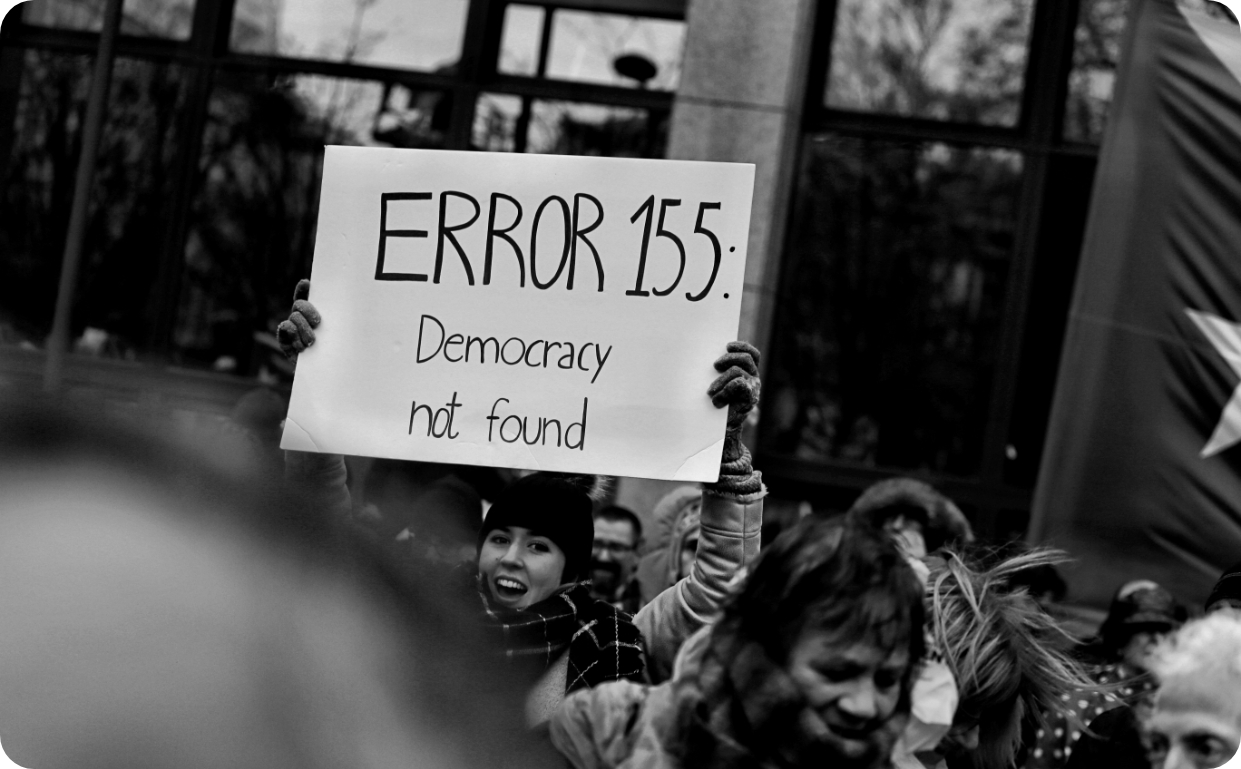 A woman holding up a sign that reads 'democracy not found'